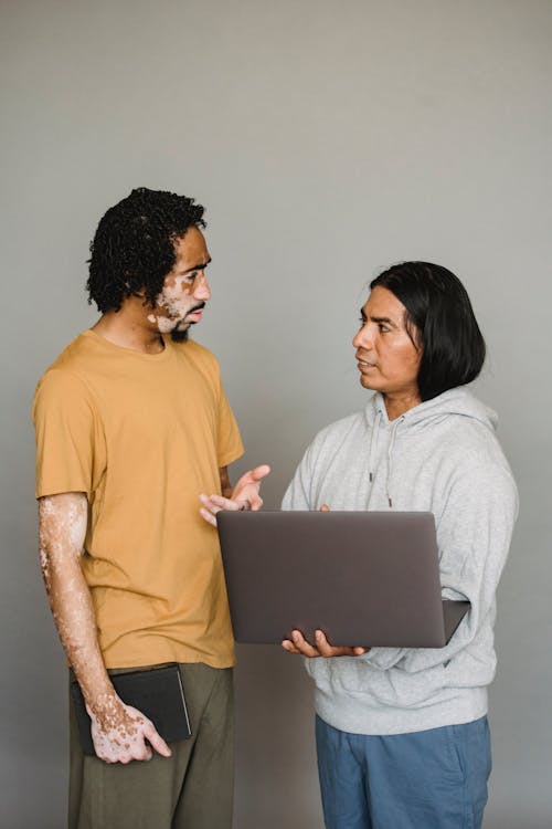 African American male with vitiligo skin talking to ethnic colleague surfing Internet during work together