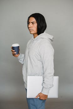 Side view of a serious man holding a coffee cup and laptop in a studio setting.