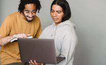 Positive multiracial coworkers discussing work together with laptop