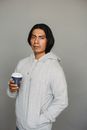 一个身穿连帽衫的男人在灰色背景下手持一次性咖啡杯的肖像照