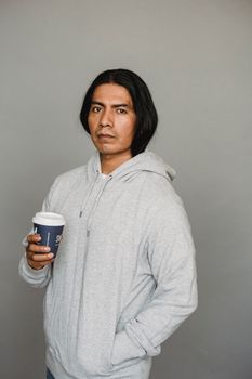 一个身穿连帽衫的男人在灰色背景下手持一次性咖啡杯的肖像照