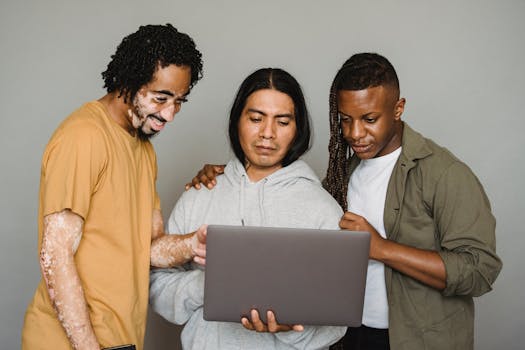 Multicultural coworkers surfing laptop while searching information together for work issues in studio against gray background