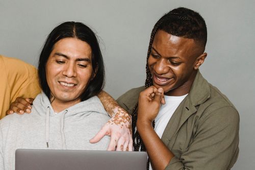 Free Delighted diverse colleagues smiling happily while working on remote project and surfing netbook together in studio Stock Photo