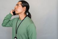 一个穿着绿色毛衣的男人在灰色背景下打电话的侧视图