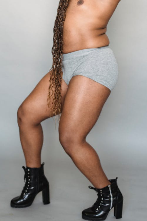 Crop faceless androgynous in boxers and shoes with high heels standing against gray background