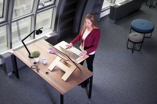 A woman working on a laptop at a standing desk in a modern office setting.