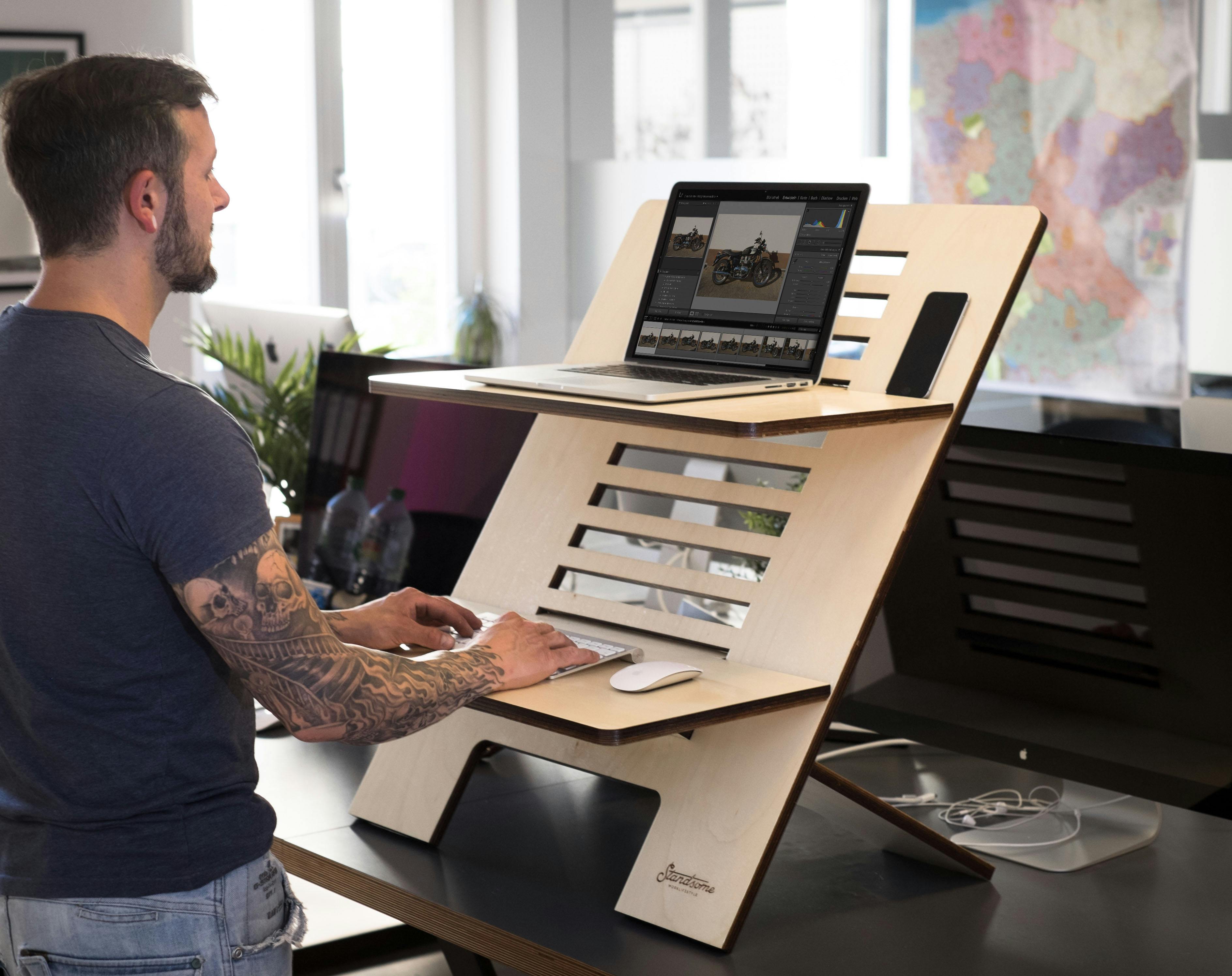 Man using a laptop on a modern standing desk in a bright office setting.