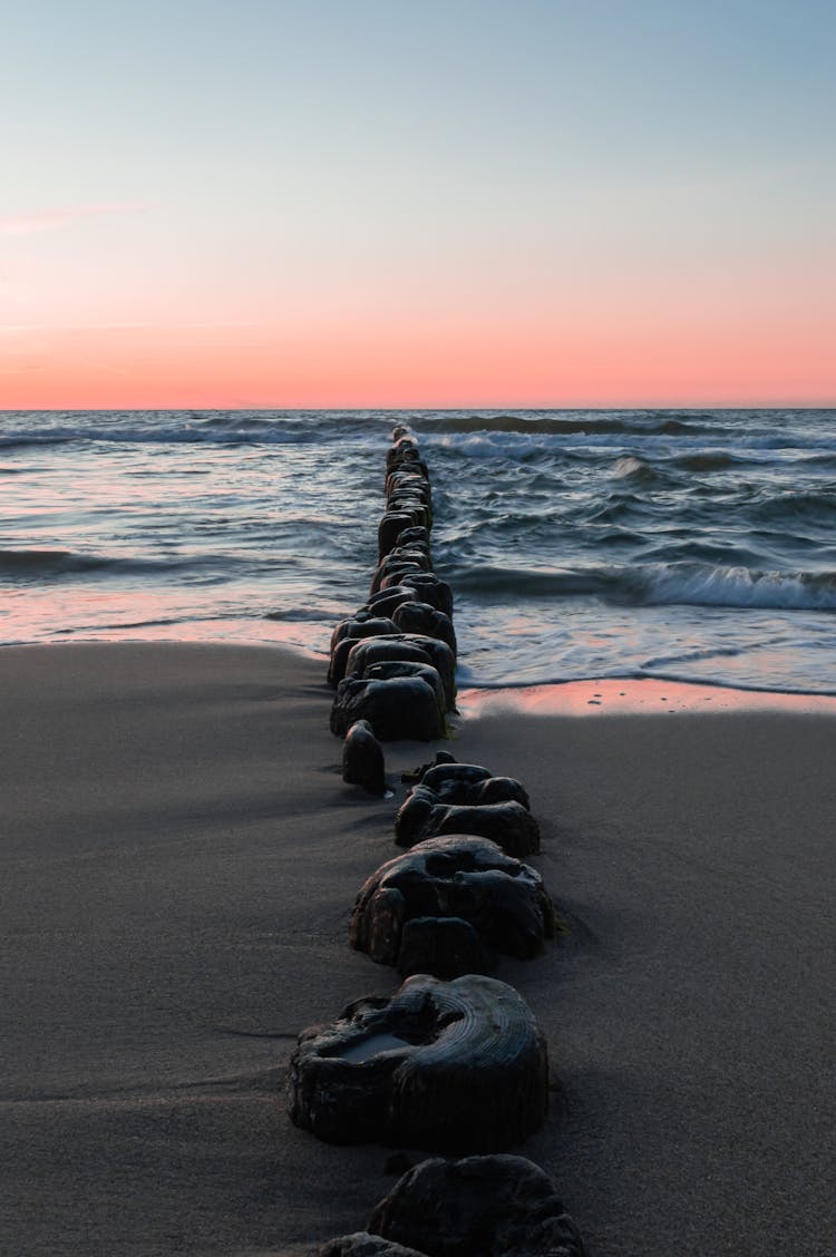 Stone Pier On Sandy Sea Shore At Sunset