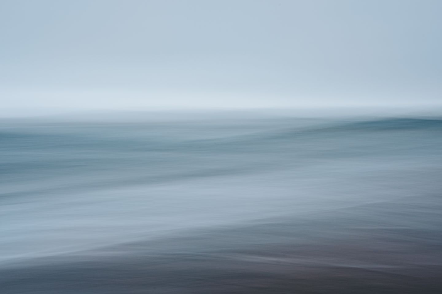 Long-exposure blur of a calm blue-gray sea meeting a pale sky