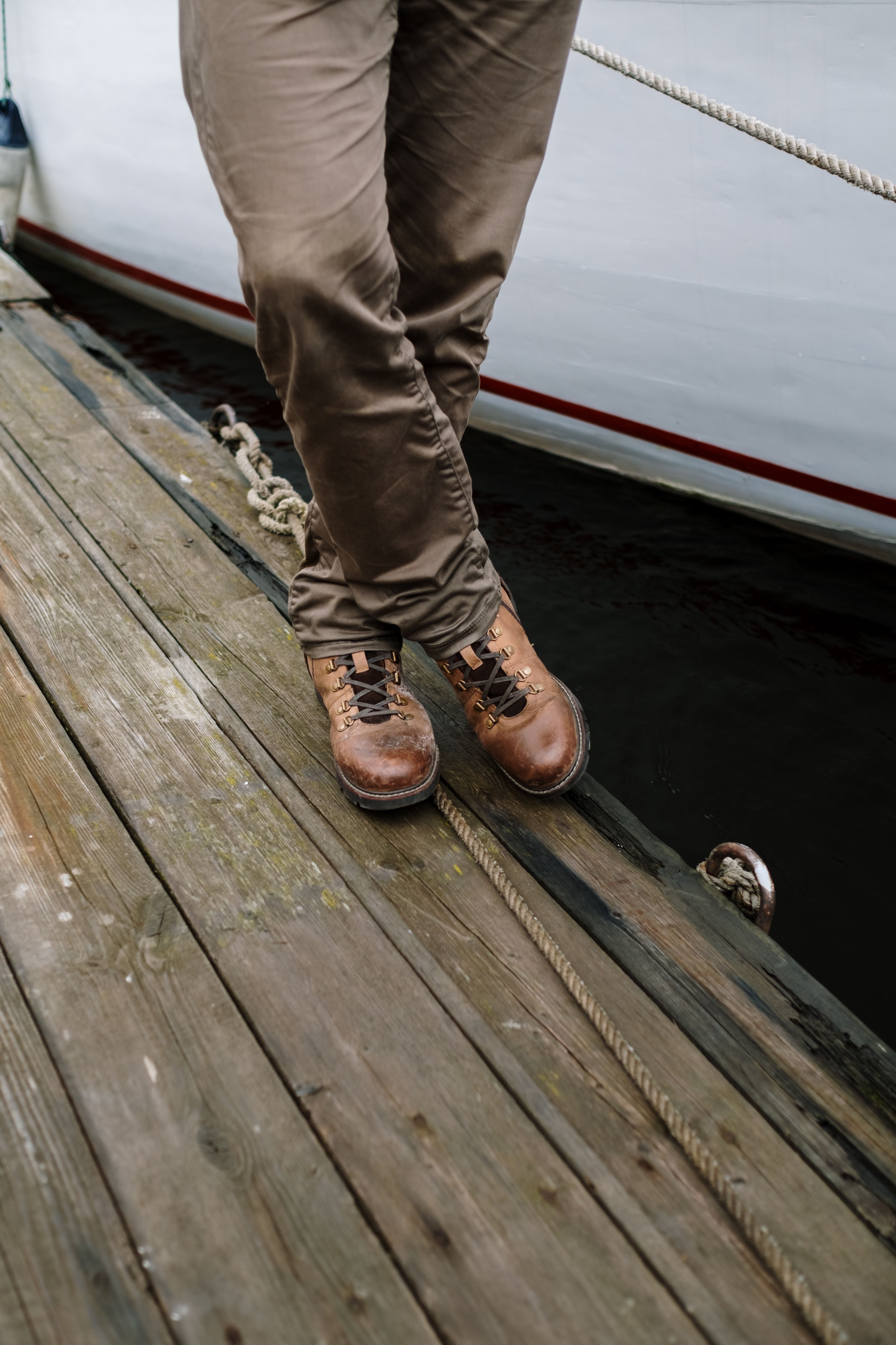 A person wearing leather boots stands on a wooden dock beside a boat.