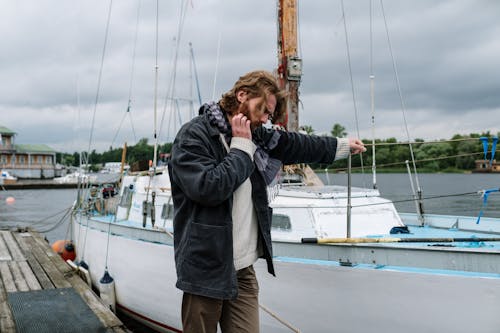 A Man Standing on a Wooden Dock Near a Yacht on a Harbor