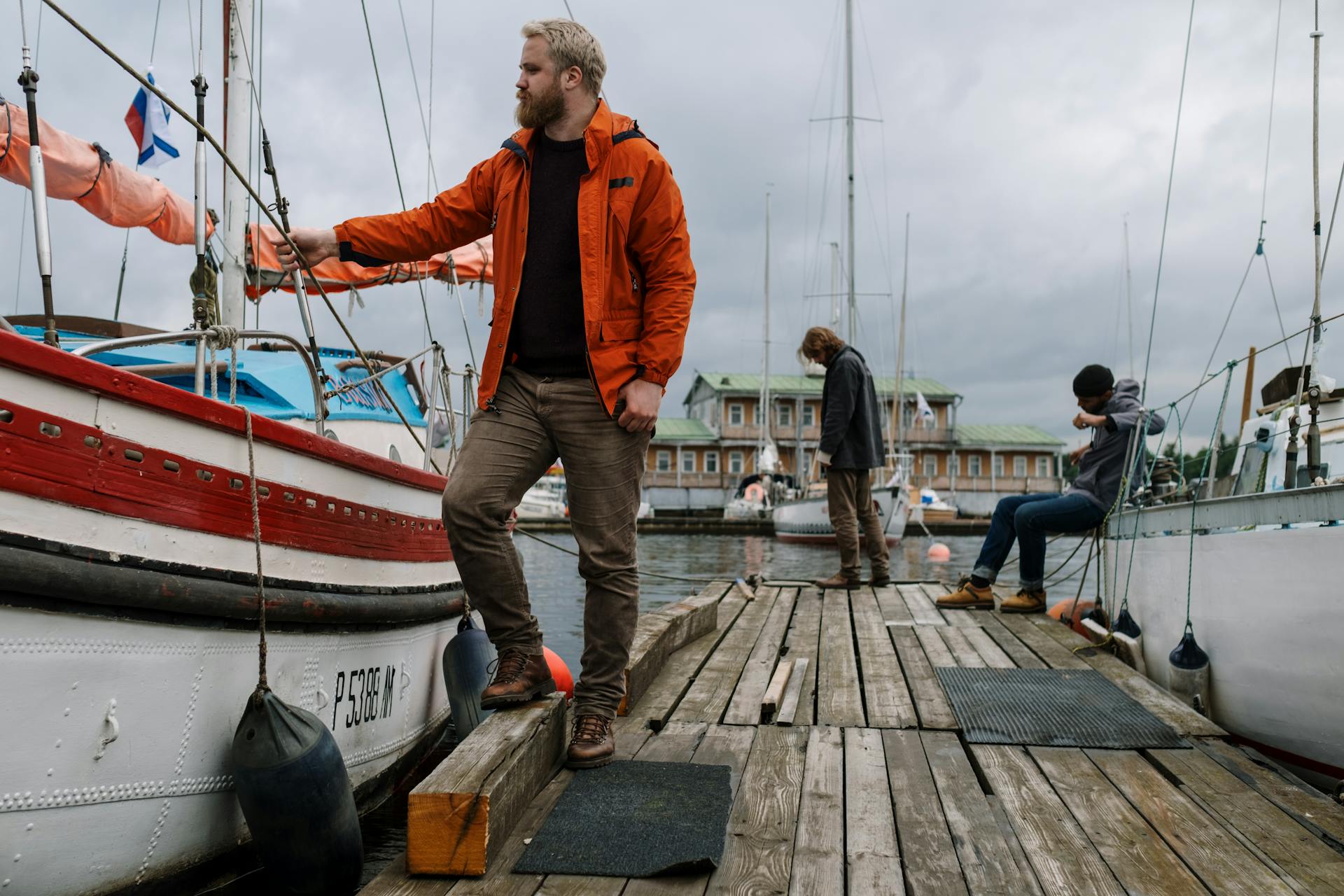 Men on a dock with boats on a cloudy day in a harbor, showcasing a nautical lifestyle.