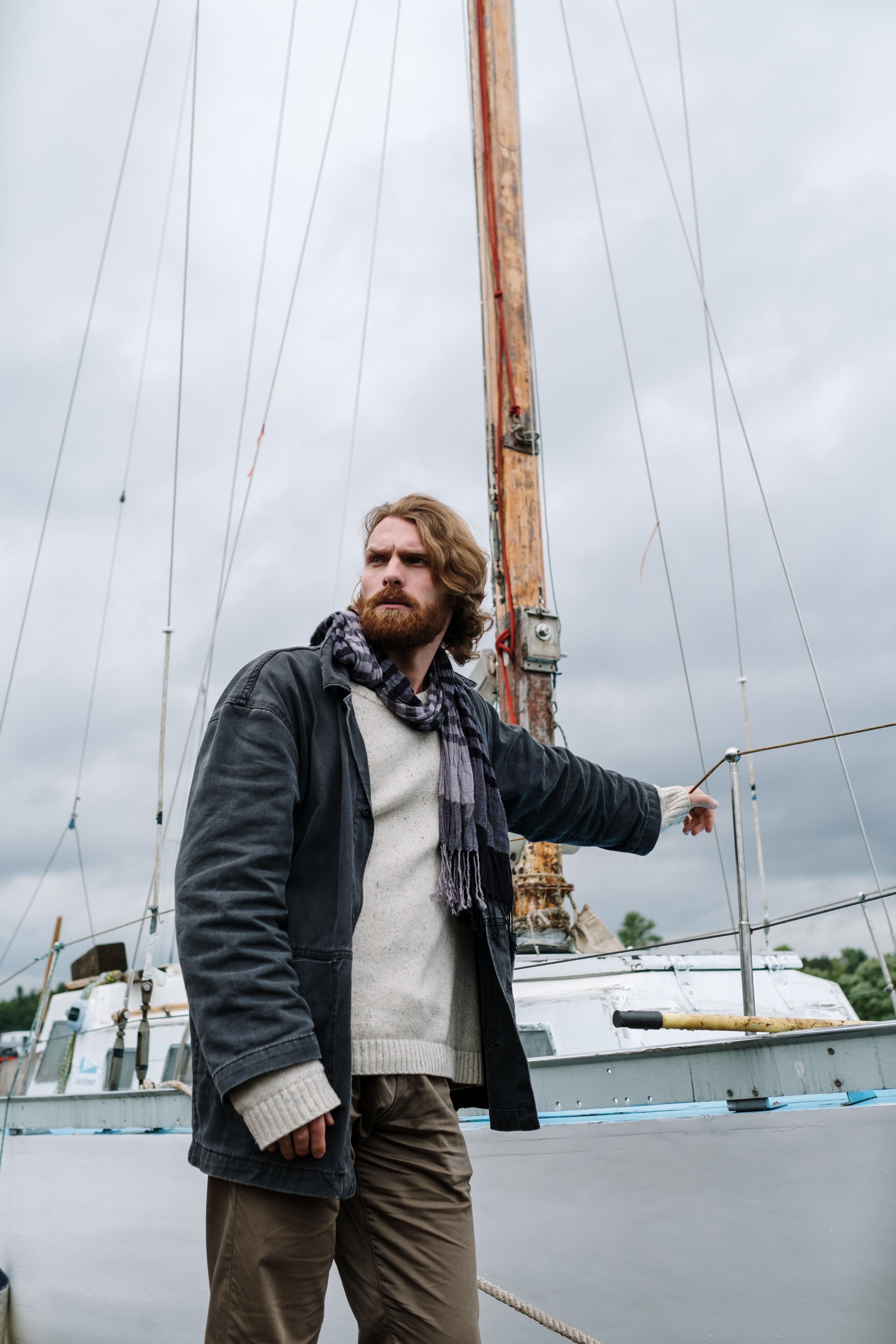 Adult man in casual clothing standing beside a sailboat on a wooden dock, looking into the distance.