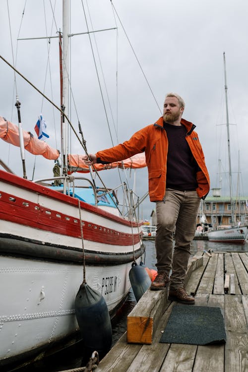 Man in Orange Jacket Standing Beside a Docked Boat 