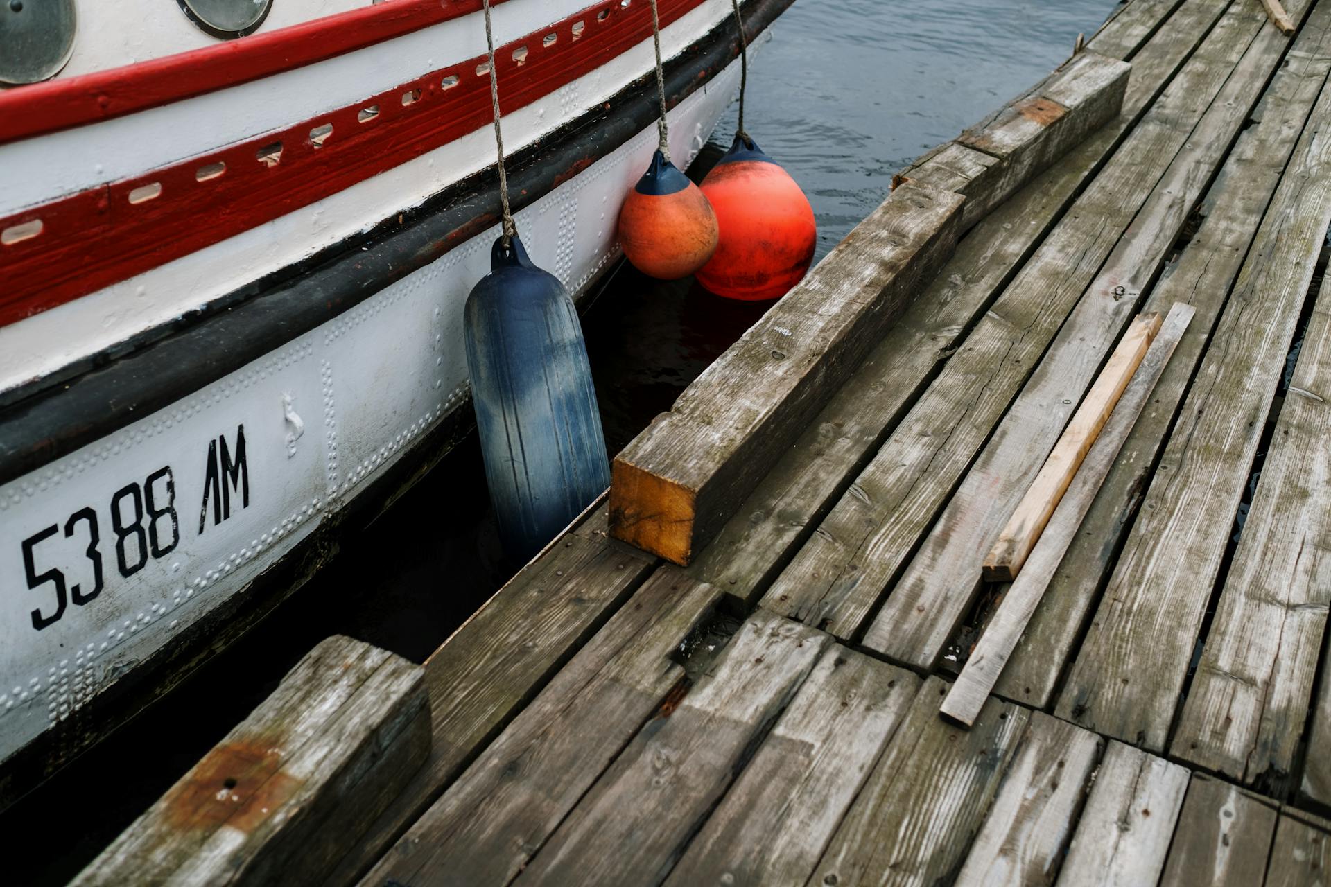 View of a wooden dock with colorful buoys and moored boat in a harbor setting.