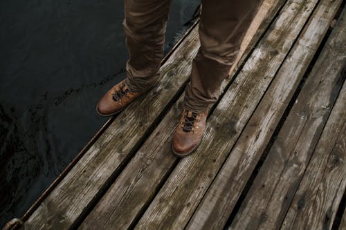 茶色の木製のドックに立っている茶色の革のブーツの人
