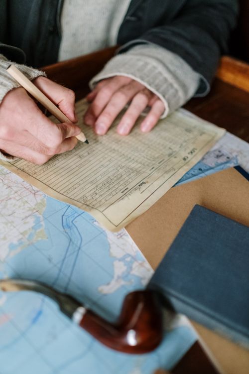Free Hands writing on paper, surrounded by maps and a pipe, suggesting navigation or planning. Stock Photo