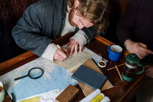 Free Adult man focused on sketching nautical plans at a cozy wooden table. Stock Photo