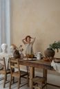 Young contemplative female carver touching hair and looking away near table with bust and potted plants
