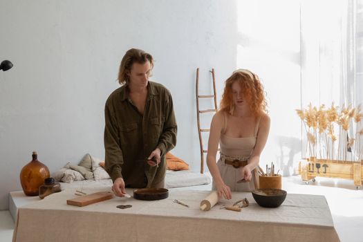 Young man with female partner in casual clothes preparing pottery tools at table in workroom