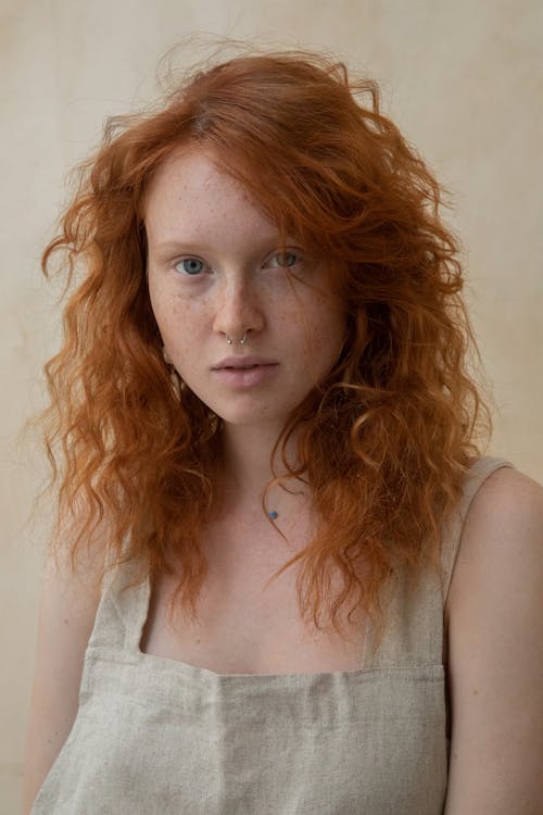 Young unemotional female in linen apparel with red head looking at camera in daytime