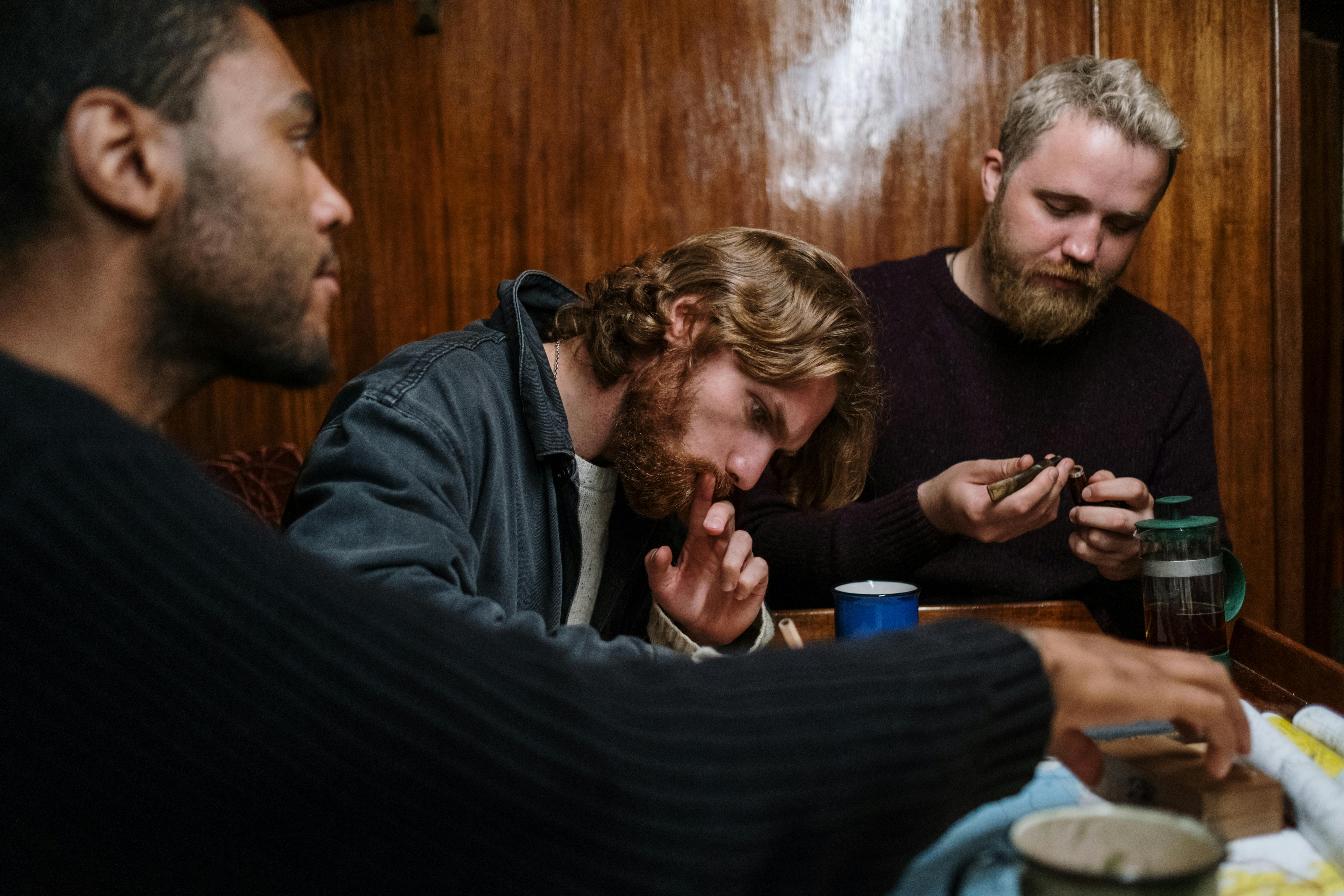Three men seated at a table inside a wooden cabin, engaged in thoughtful discussion.