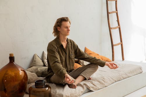 Young mindful barefoot male with closed eyes sitting in Padmasana pose while practicing yoga at home