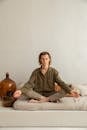 Young reflective barefoot male sitting in Padmasana pose with closed eyes on cozy mattress in house