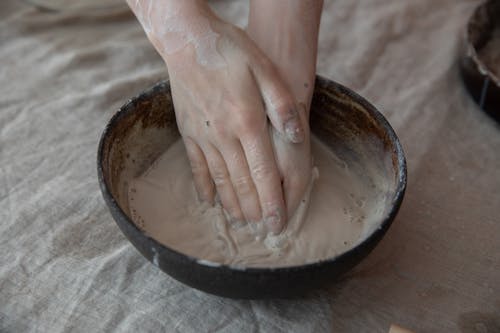 From above of crop anonymous craftsperson mixing clay in round shaped bowl in workroom