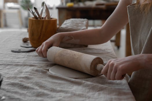 Close-up of a craftsperson rolling clay on a table, showcasing pottery making process.
