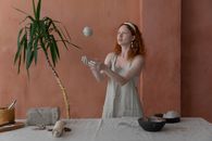 Young skilled female ceramist wearing light apron throwing clay ball while making ceramic products in modern workshop