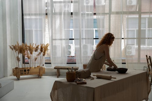 Side view faceless female wearing apron placing clay slab on baking pan while making earthenware in contemporary studio