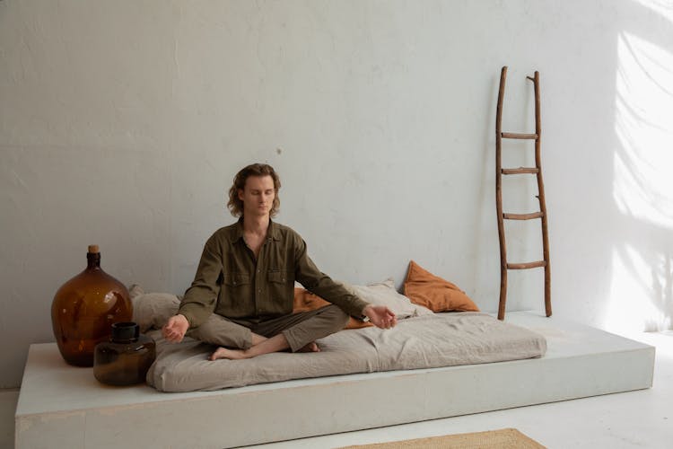 Peaceful Man Meditating On Bed In Lotus Pose