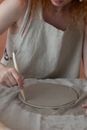 Unrecognizable female master in apron cutting round piece of clay with knife while making pottery during work in professional studio
