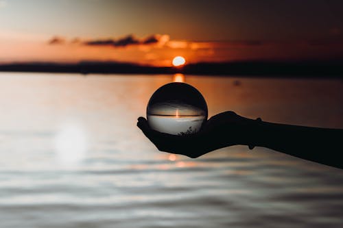 A Person Holding a Glass Ball at Sunset