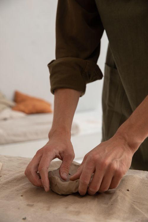 Free Crop unrecognizable craftsman in casual clothes standing at table and creating handmade thing from clay in creative studio Stock Photo