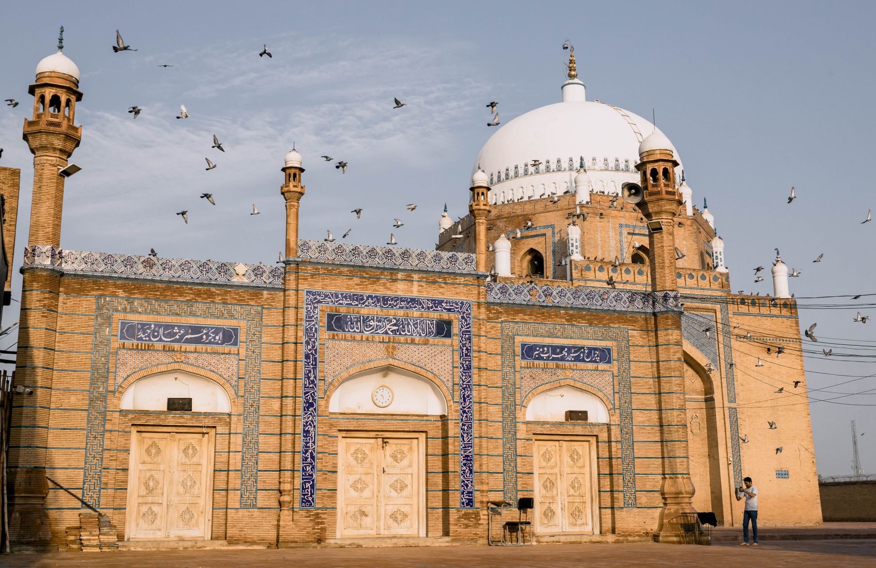 A stunning view of the Bahauddin Zakariya Shrine in Multan with flying pigeons against a clear sky.