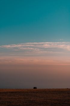 A tranquil view of a sunset sky over an expansive farm field with a single hay bale.