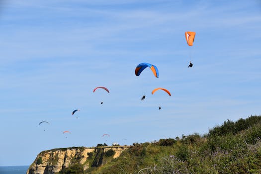 A group of paragliders soar over scenic cliffs on a clear day, showcasing vibrant parachute colors.