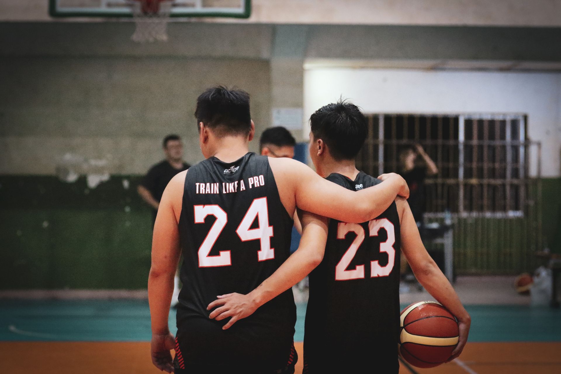 Two basketball players wearing jerseys embrace, symbolizing teamwork and camaraderie after training.