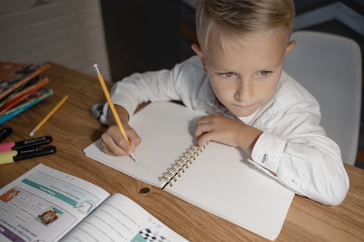 Child focused on homework, writing in a notebook with study materials nearby.