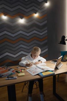 A young boy focused on his homework, using a tablet and surrounded by school books, in a cozy indoor setting.