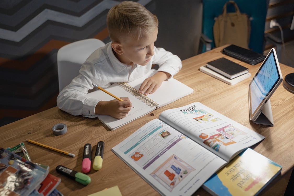 Boy in White Long Sleeve Shirt Writing on White Paper