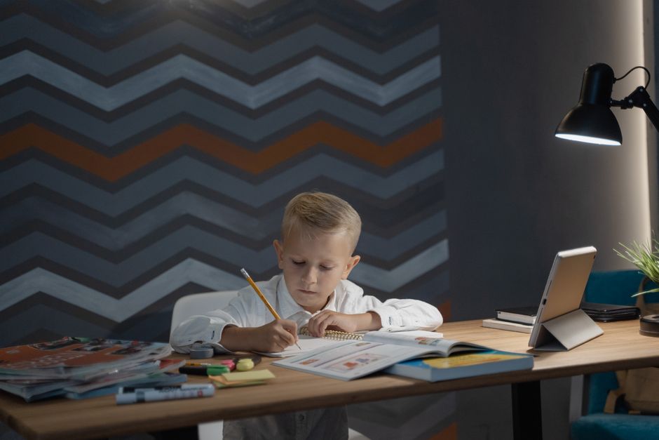 Photo by Tima Miroshnichenko on Pexels A child focuses on his homework at a desk with a tablet and lamp, promoting education at home. - Photo by Tima Miroshnichenko on Pexels