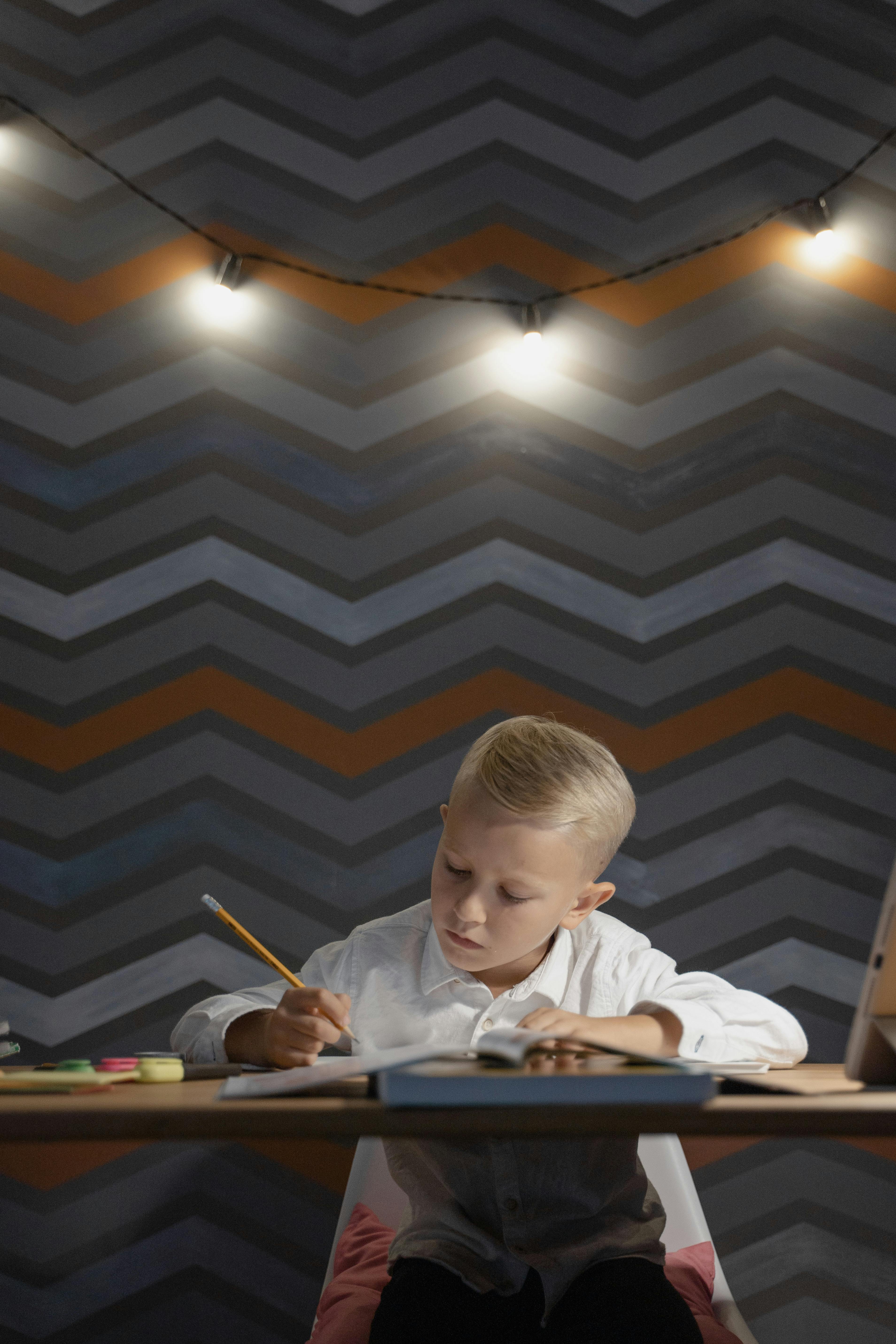 boy in white long sleeve shirt holding pen writing on white paper