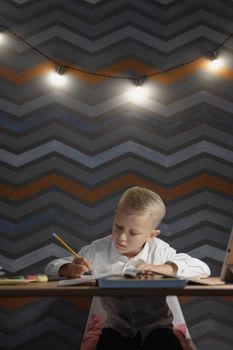A young boy diligently doing homework at a desk under warm lights.