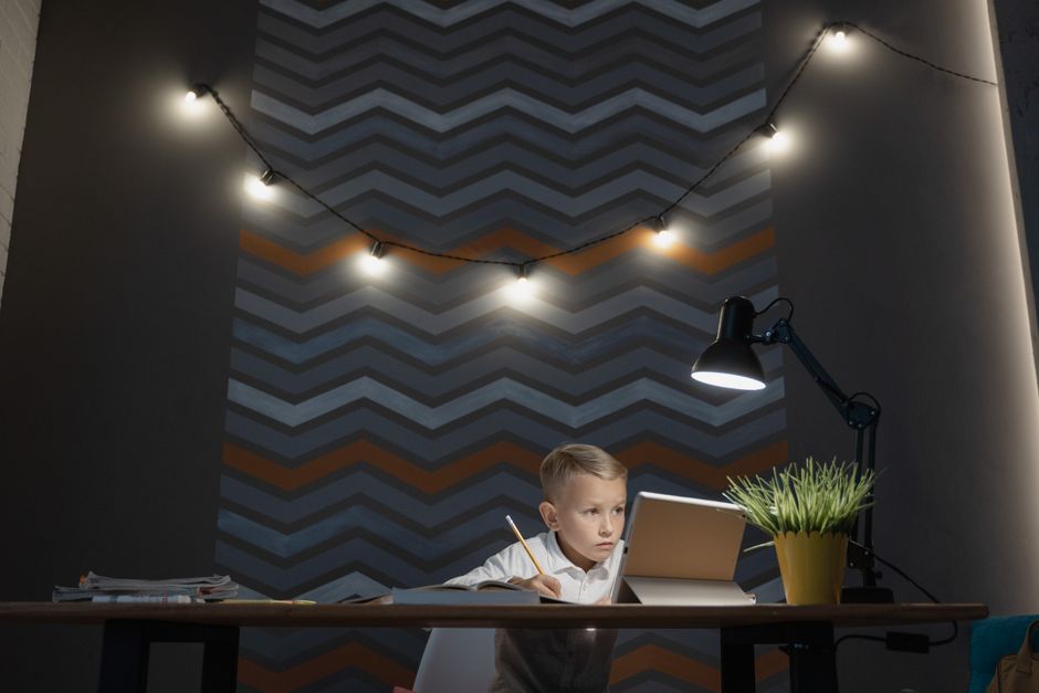A young boy intensely studying with a tablet under a lamp on a modern chevron-patterned wall.