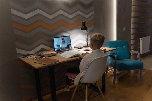 Young boy attending virtual class at home desk with laptop, focusing on education.