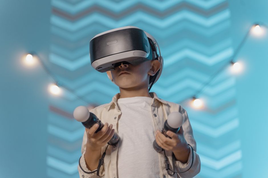 VRゴーグルとコントローラーを持つ子供が屋内でバーチャルリアリティゲームを楽しんでいる。