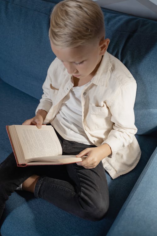 
A Boy Reading a Book while Sitting on a Sofa